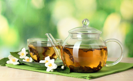Заварочный чайник и чашки с чаем, рядом лежат цветы жасмина