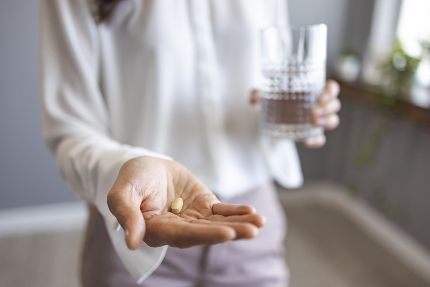 Женщина держит таблетку на ладони. В другой руке стакан с водой