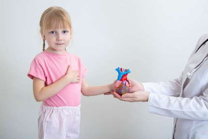 Девочка стоит, положив руку на грудь, второй берет макет сердца, который ей протягивает врач.