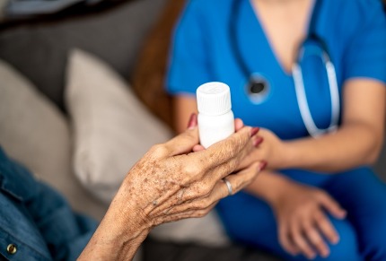 Пожилая женщина держит в руке баночку с лекарствами, рядом сидит врач