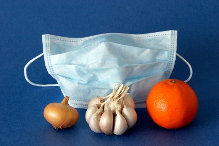 Различные народные средства от простуды на фоне медицинской маски: лук, чеснок, мандарин.