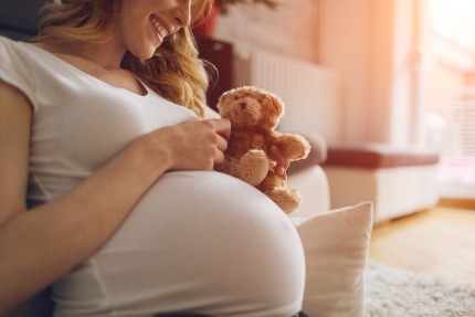 Беременная женщина держит в руке игрушечного медведя.