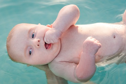 Грудной малыш лежит в бассейне на руках у мамы.