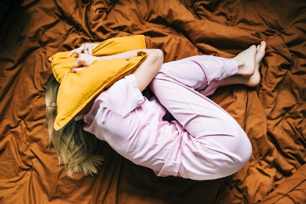 Женщина лежит на кровати, закрыв голову подушкой.