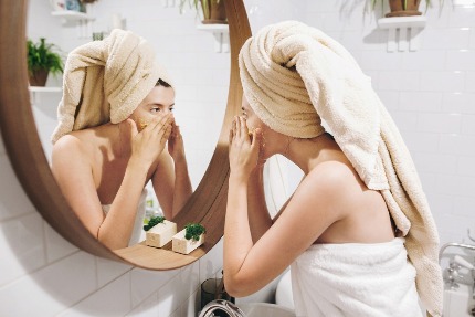 Женщина наносит косметическое средство на лицо у зеркала.