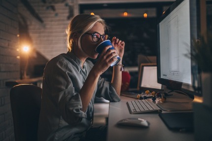 Женщина работает ночью за компьютером и пьет кофе