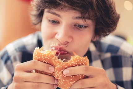 Подросток ест гамбургер.