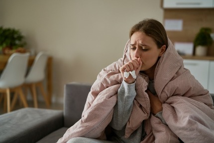 Простуженная женщина кашляет, завернувшись в одеяло.