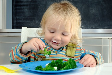 Ребенок ест вареную брокколи.