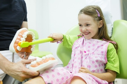 Девочка учится правильно чистить зубы в кабинете стоматолога.
