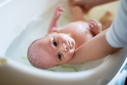 Новорожденного ребенка купают в ванночке.