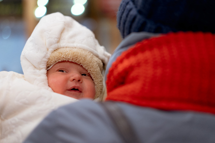 Тепло одетого новорожденного ребенка несут по улице на руках.
