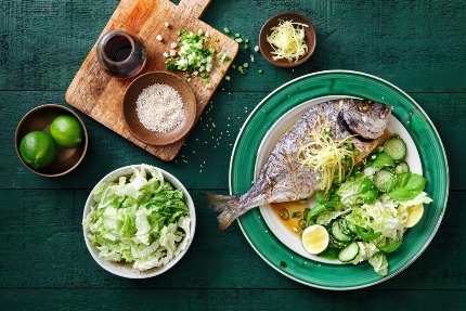 На столе стоит приготовленная рыба и салаты