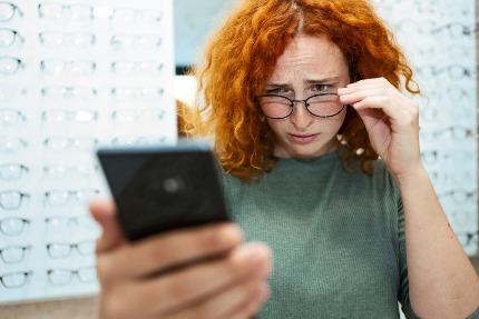 Женщина примеряет очки и смотрит в телефон.