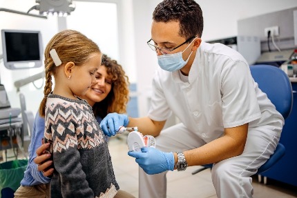 Стоматолог показывает девочке, как правильно чистить зубы