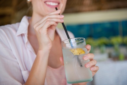 Молодая женщина пьет кокосовую воду из стакана.