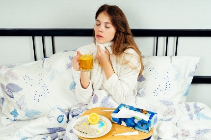 Болеющая женщина пьет чай с лимоном в кровати.