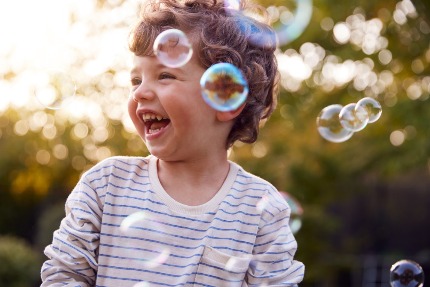 Мальчик смеется, вокруг летают мыльные пузыри