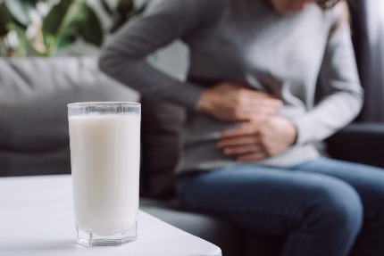 Женщина держится руками за живот, перед ней на столе стоит молоко.