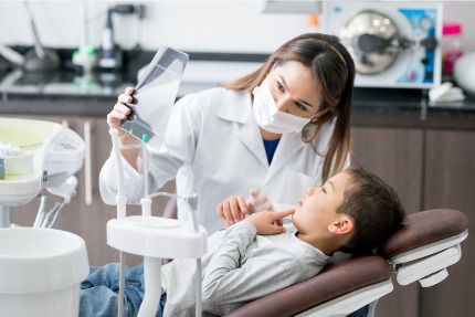 Мальчик сидит в стоматологическом кресле, рядом сидит врач.