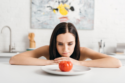 Женщина смотрит на помидор, который лежит на тарелке