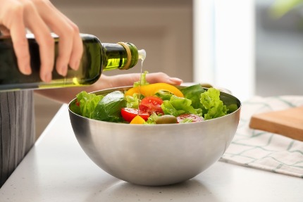 Женщина заправляет салат растительным маслом