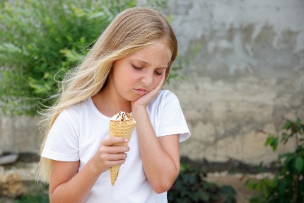 Девочка держит мороженое в одной руке, вторую положила на щеку
