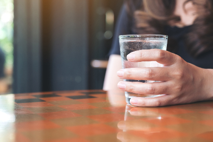 Женщина держит в руке стакан с водой.