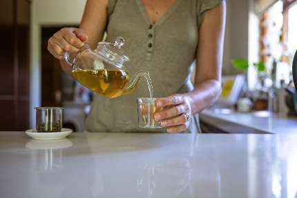 Женщина наливает в чашку травяной чай из чайника.