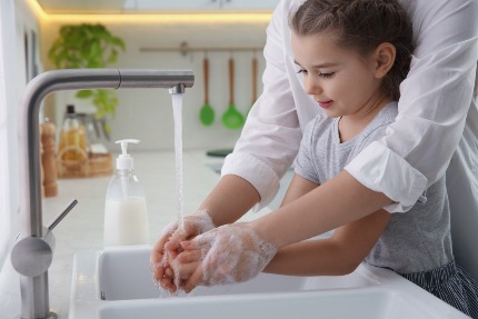 Мама учит дочь мыть руки с мылом.