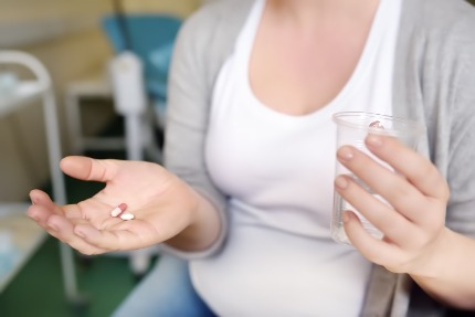 Женщина держит на ладони таблетки, в другой руке стакан с водой