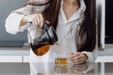 Женщина наливает травяной чай из чайника в кружку.