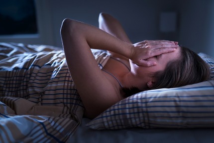 Женщина ночью лежит в кровати, закрыв лицо руками.
