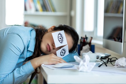 Женщина уснула за рабочим столом, на глаза наклеила бумажки с нарисованными открытыми глазами