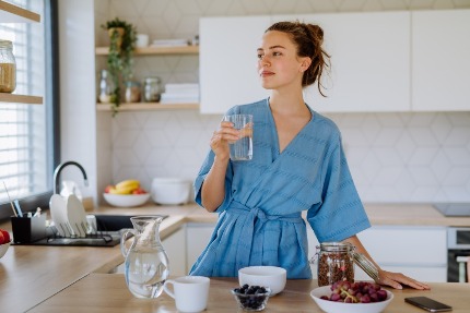 Женщина на кухне держит в руках стакан воды.